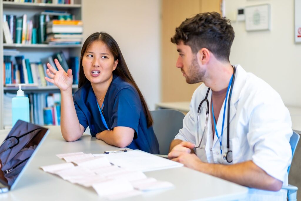 A doctor and a nurse review a patient chart together at a hospital library table.