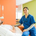 A nurse smiles while examining a patient on a hospital bed.