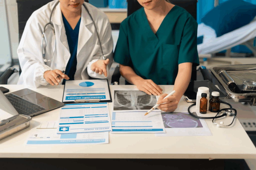 Two medical professionals looking at paperwork next to a computer.