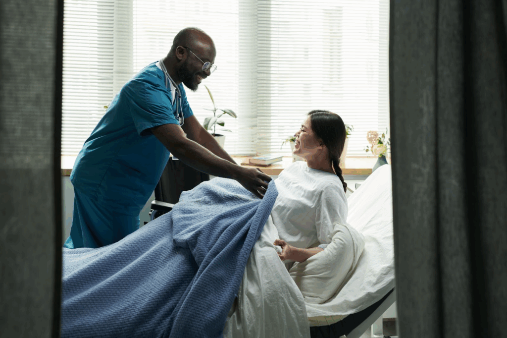 A nurse drapes a blanket over a pregnant patient in her hospital bed.